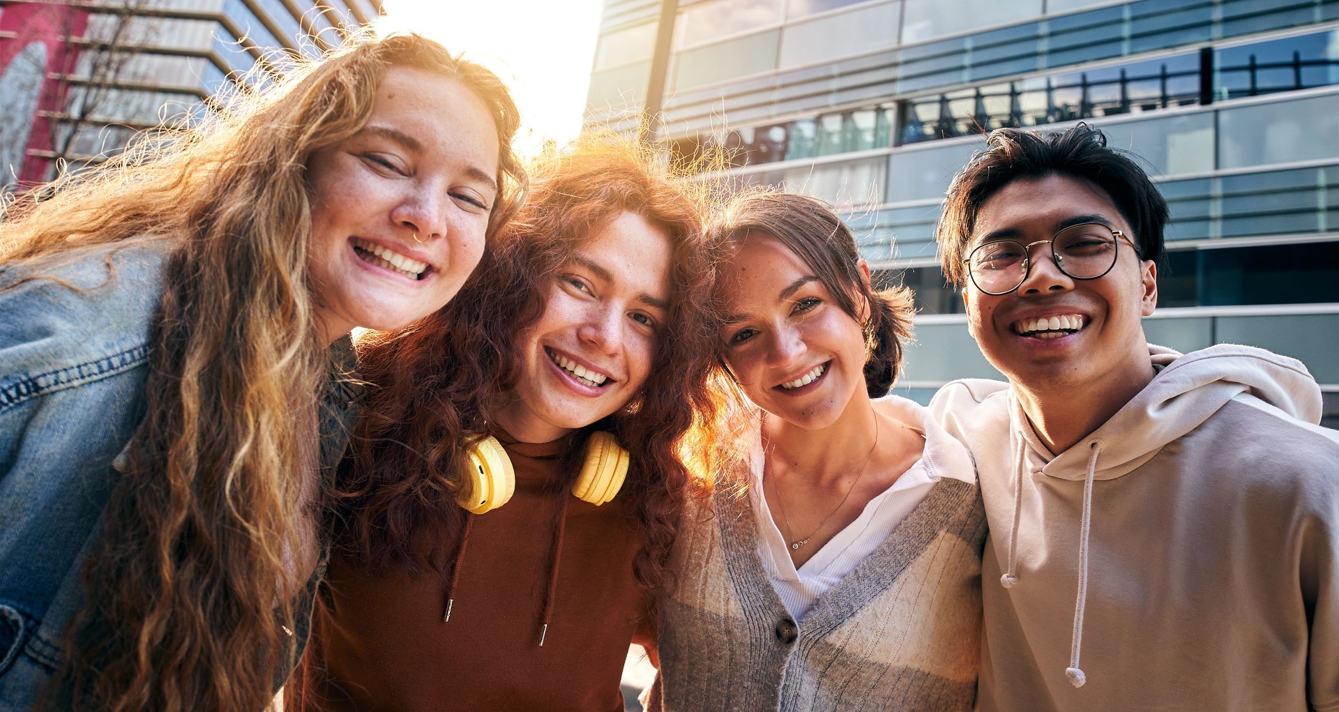 Erasmus International university students looking at camera happily hugging each other outdoors.